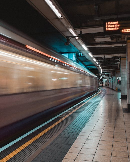 This image shows a moving train arriving at an underground station platform with beige and brown exterior, captured in motion blur indicating high speed. The platform features beige tiled flooring wit